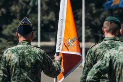 2 militairen met een oranje vaandel tussen hen in.