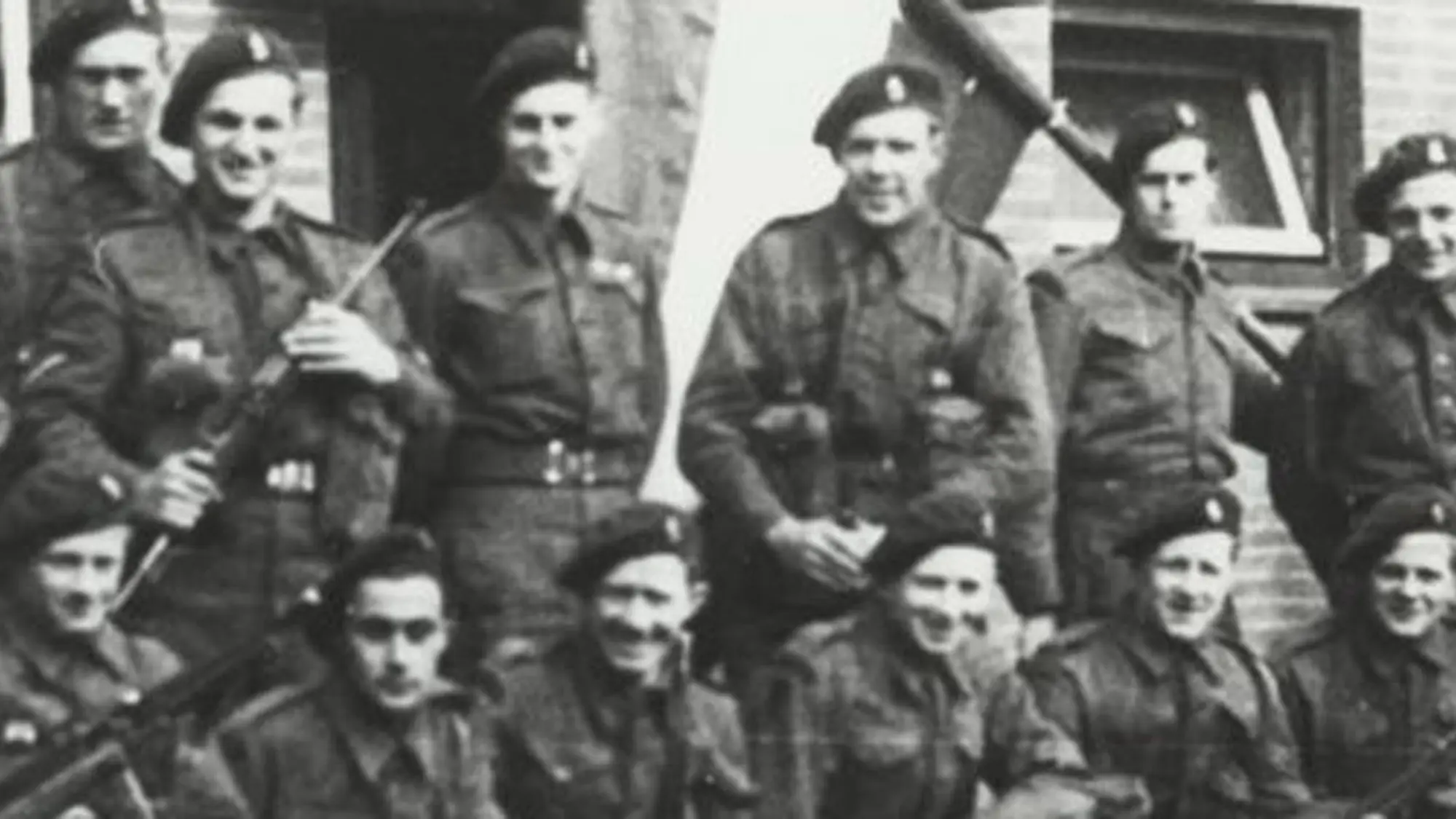 Oude zwart-witfoto van groep militairen waarvan enkele een wapen vasthouden.