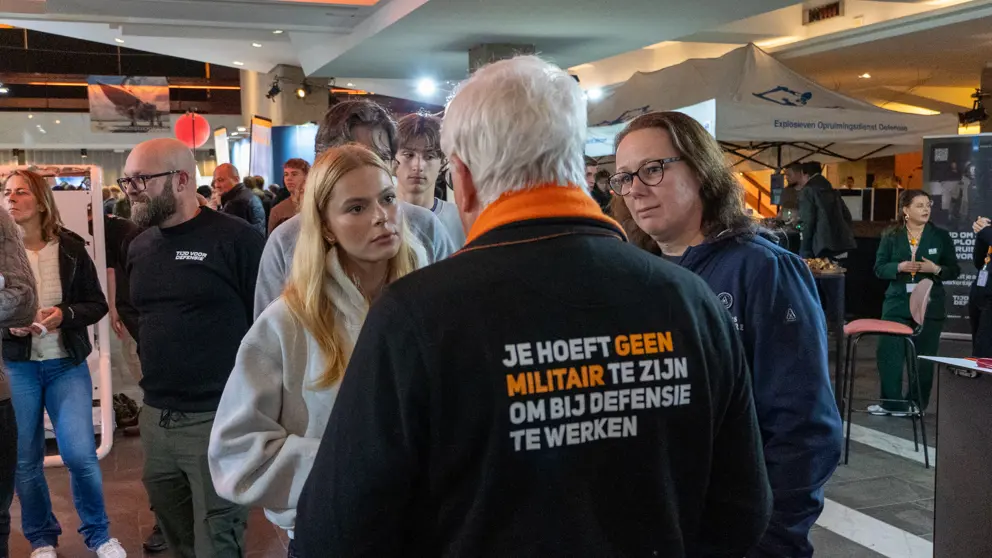 2 bezoekers luisteren naar een defensiemedewerker.