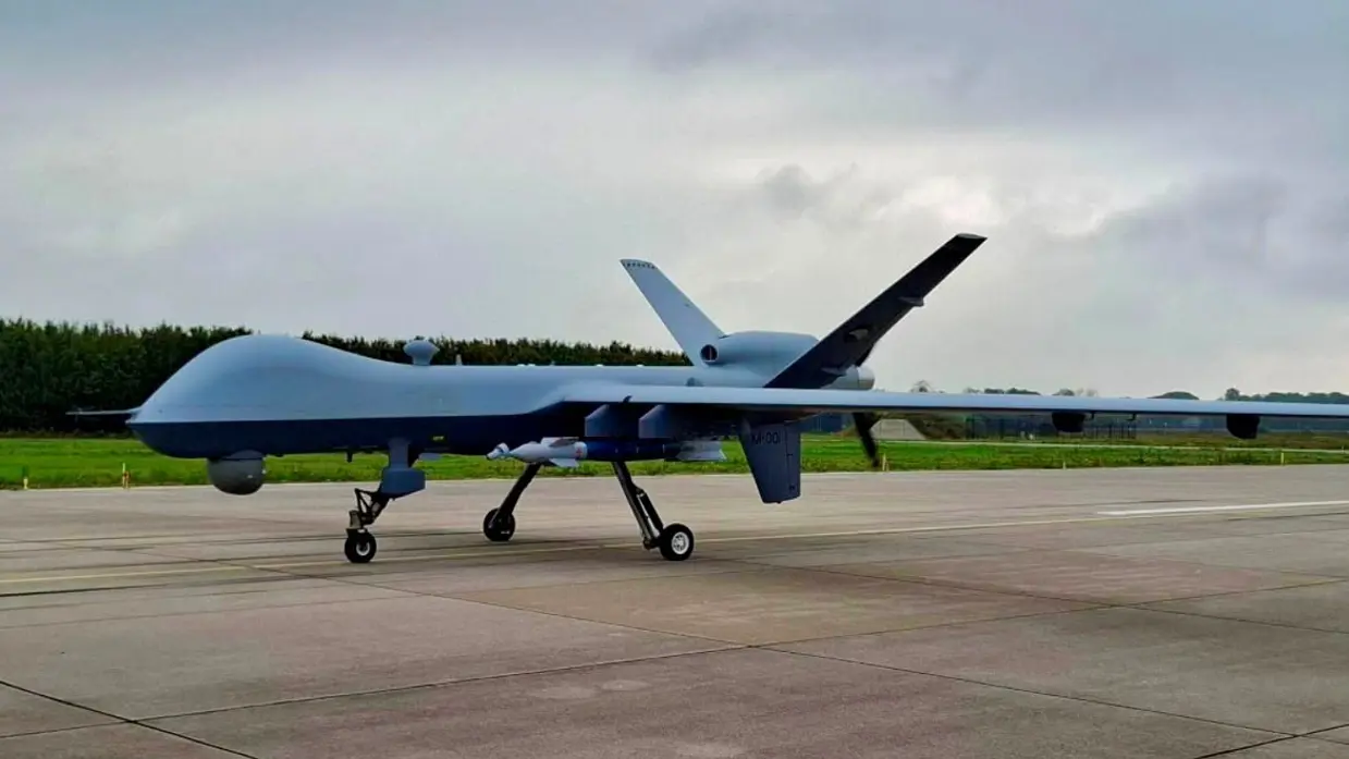 Een bewapende MQ-9 Reaper op een platform met op de achtergrond gras en bomen.