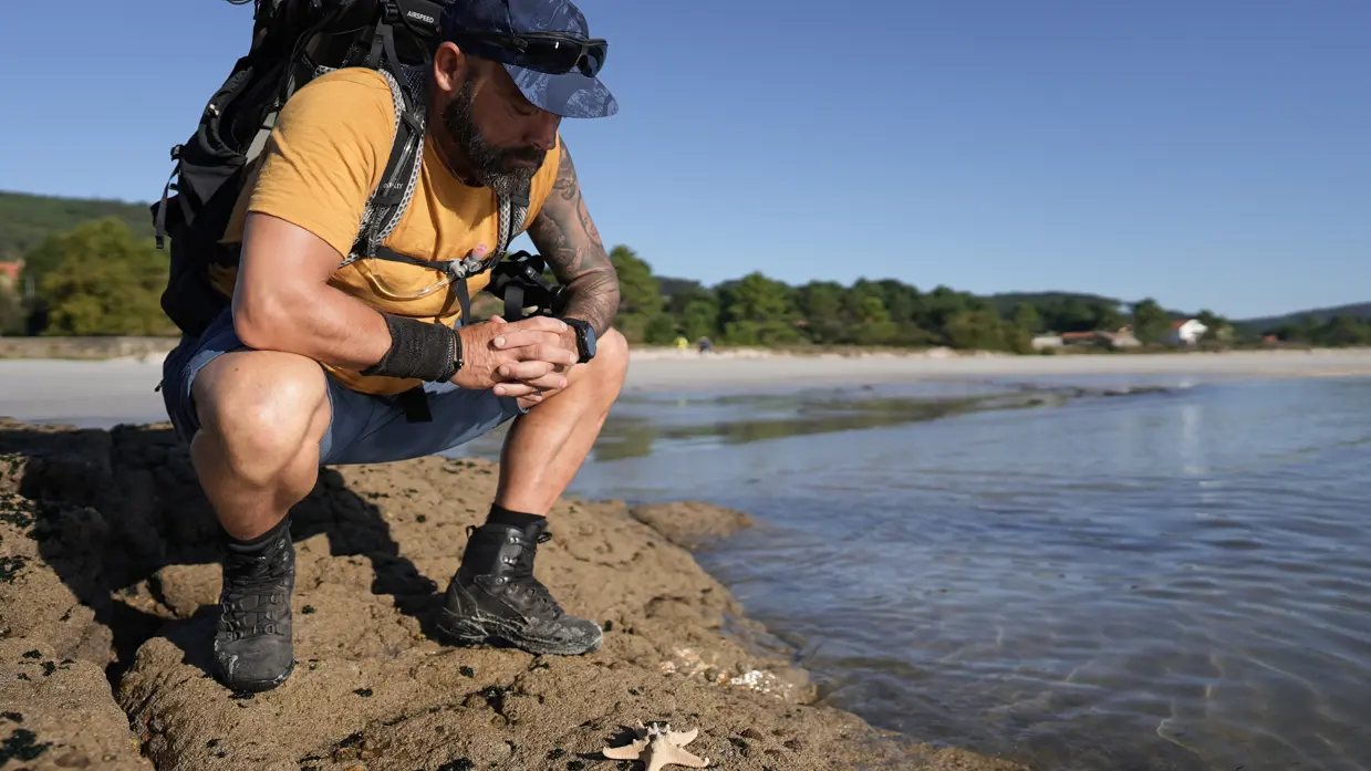 René zit gehurkt bij een zeester aan het water 