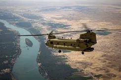 Chinook-transporthelikopter boven een meanderende rivier en woestijngebied.