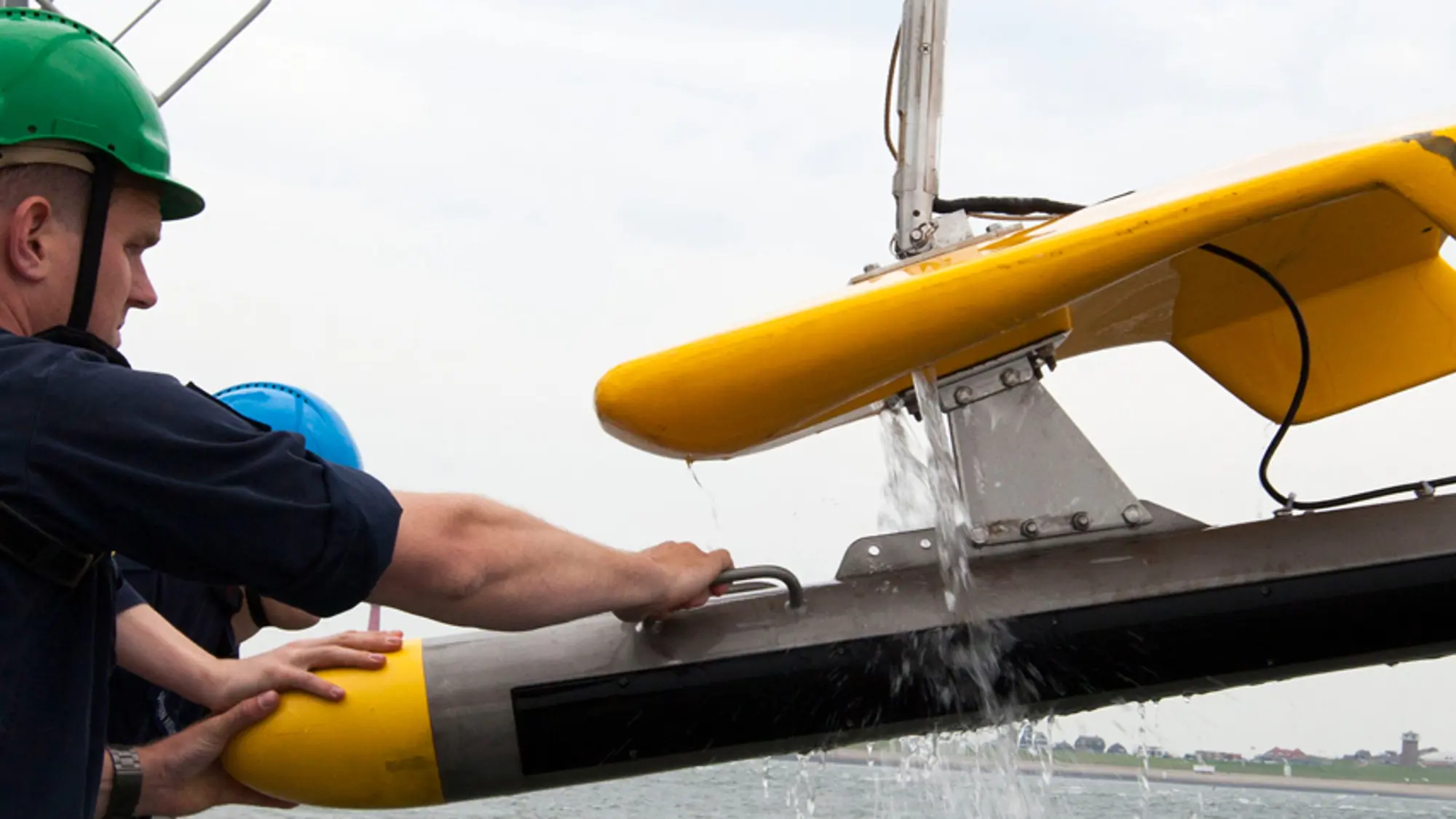 Medewerker met groene helm op takelt onderwaterdrone uit het water.