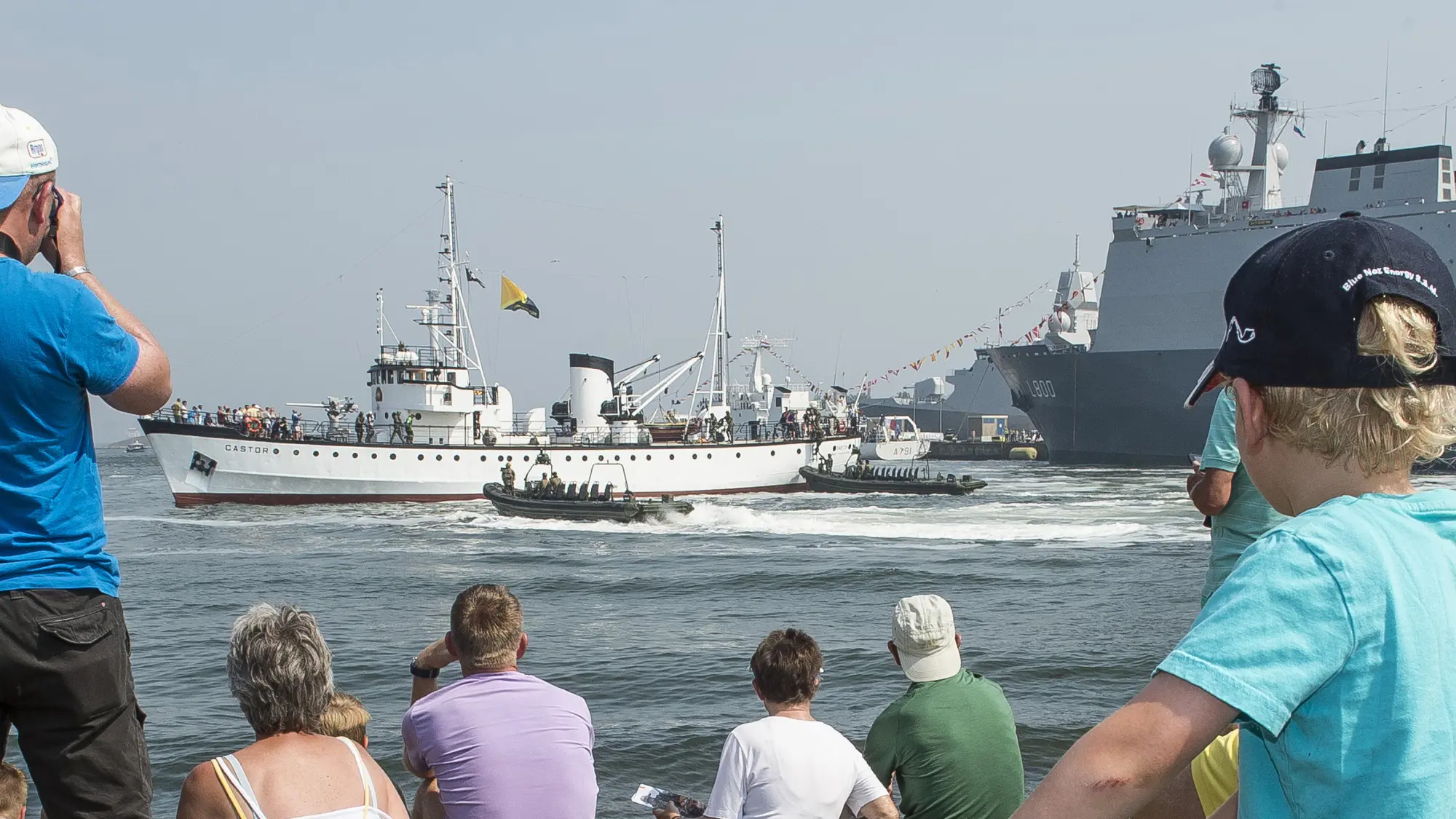 Bezoekers tijdens de Marinedagen kijken vanaf de wal naar marineschepen op het water.