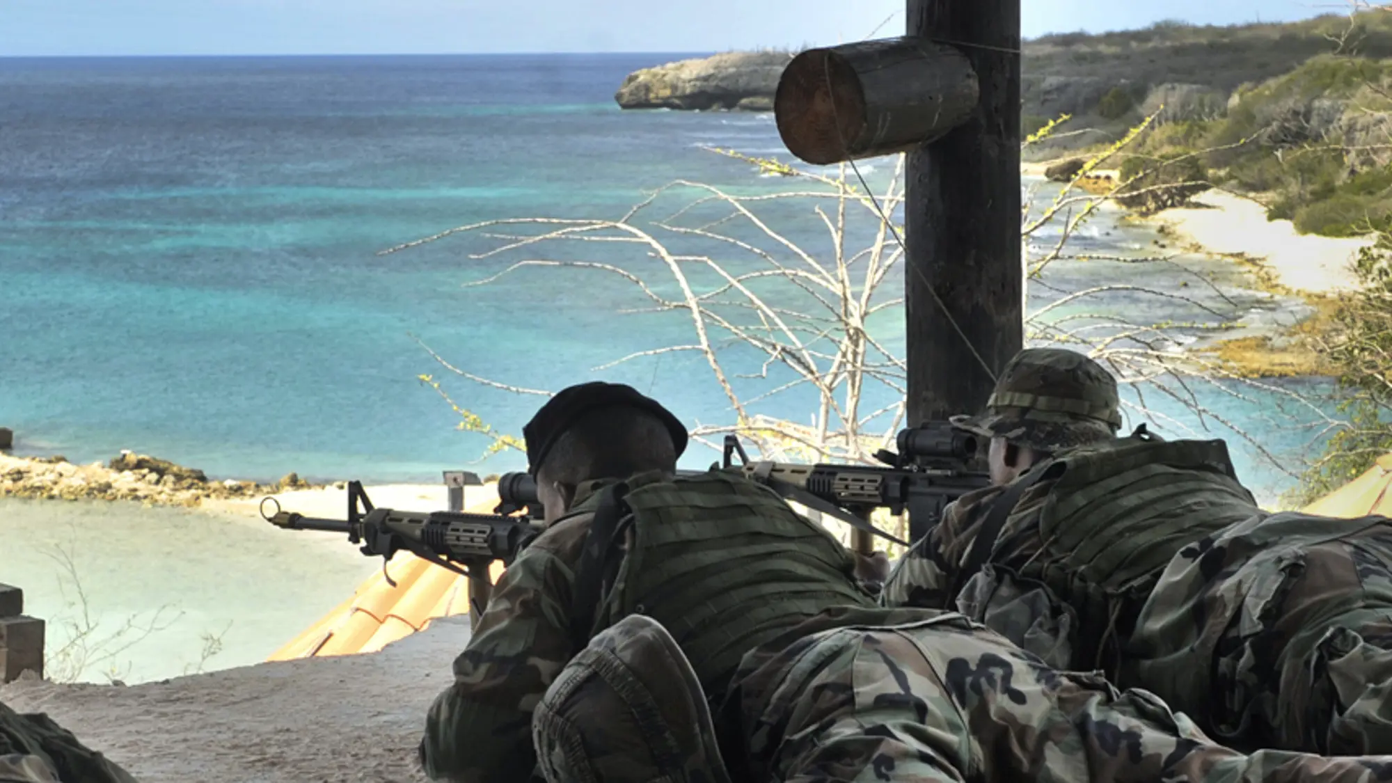 Militairen liggen tijdens een oefening op de grond achter hun geweer dat richting zee is gericht.