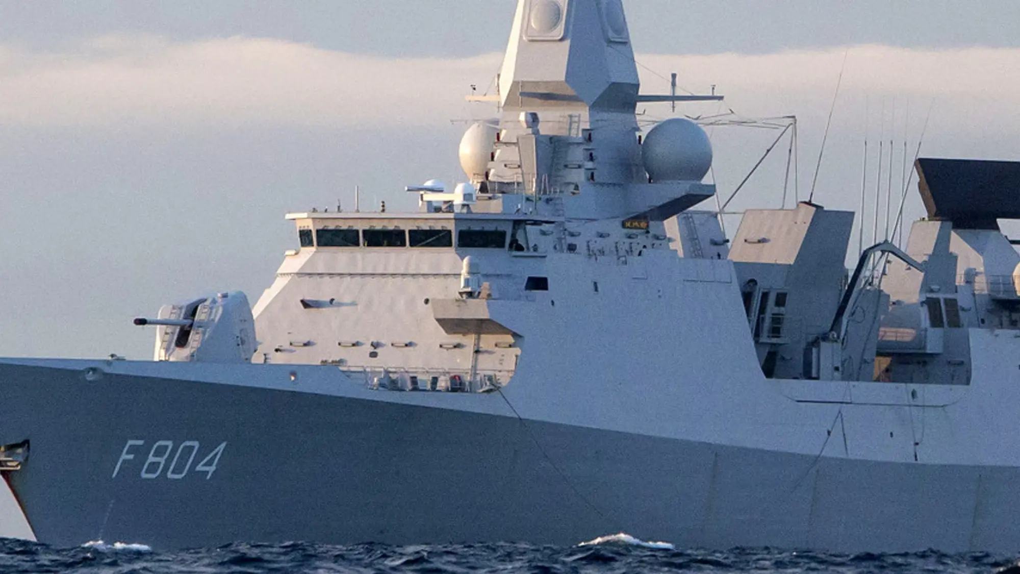 Zr.Ms. De Ruyter op zee met op de achtergrond besneeuwde bergen.