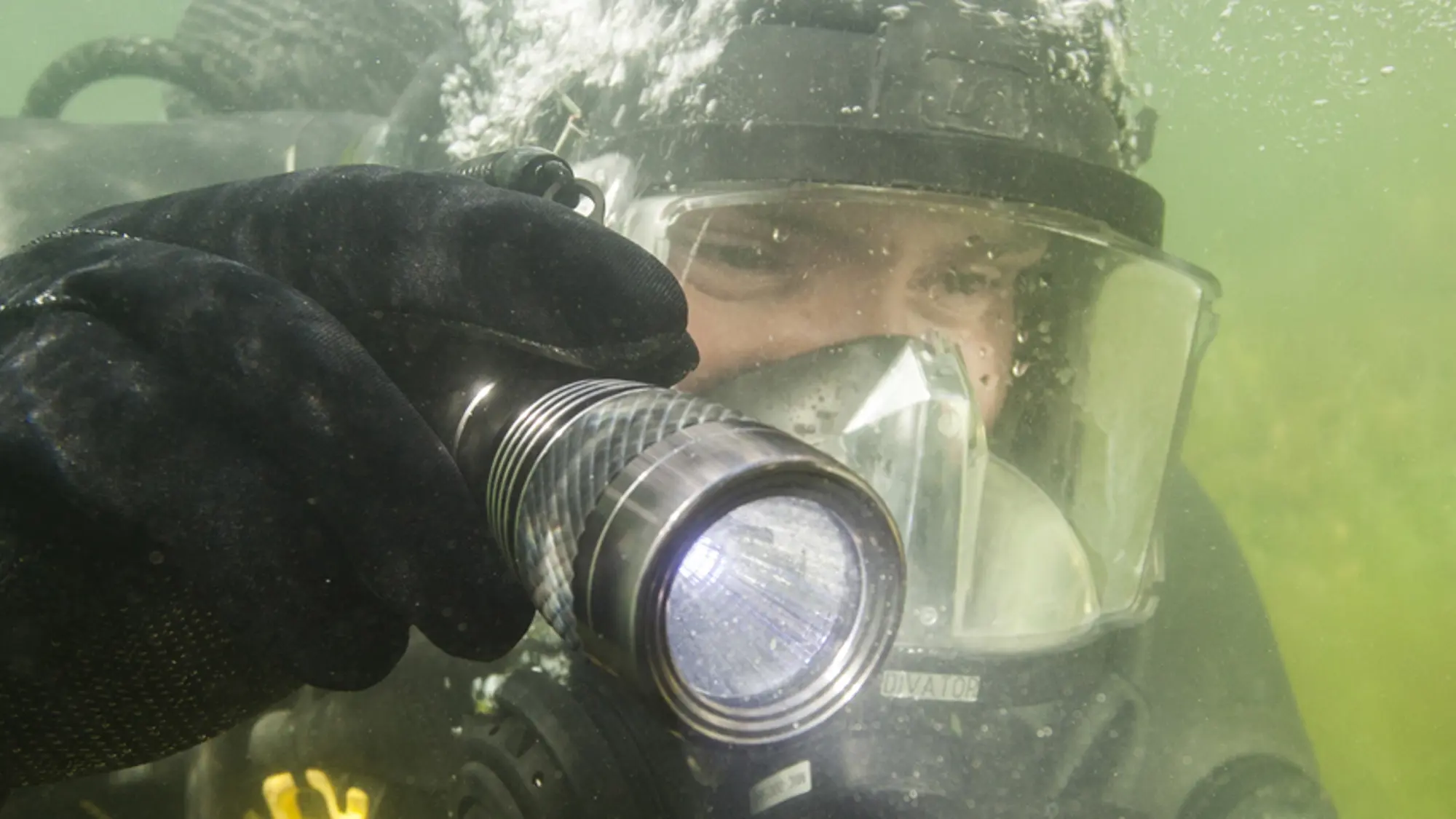 Duiker schijnt met zaklantaarn onder water.