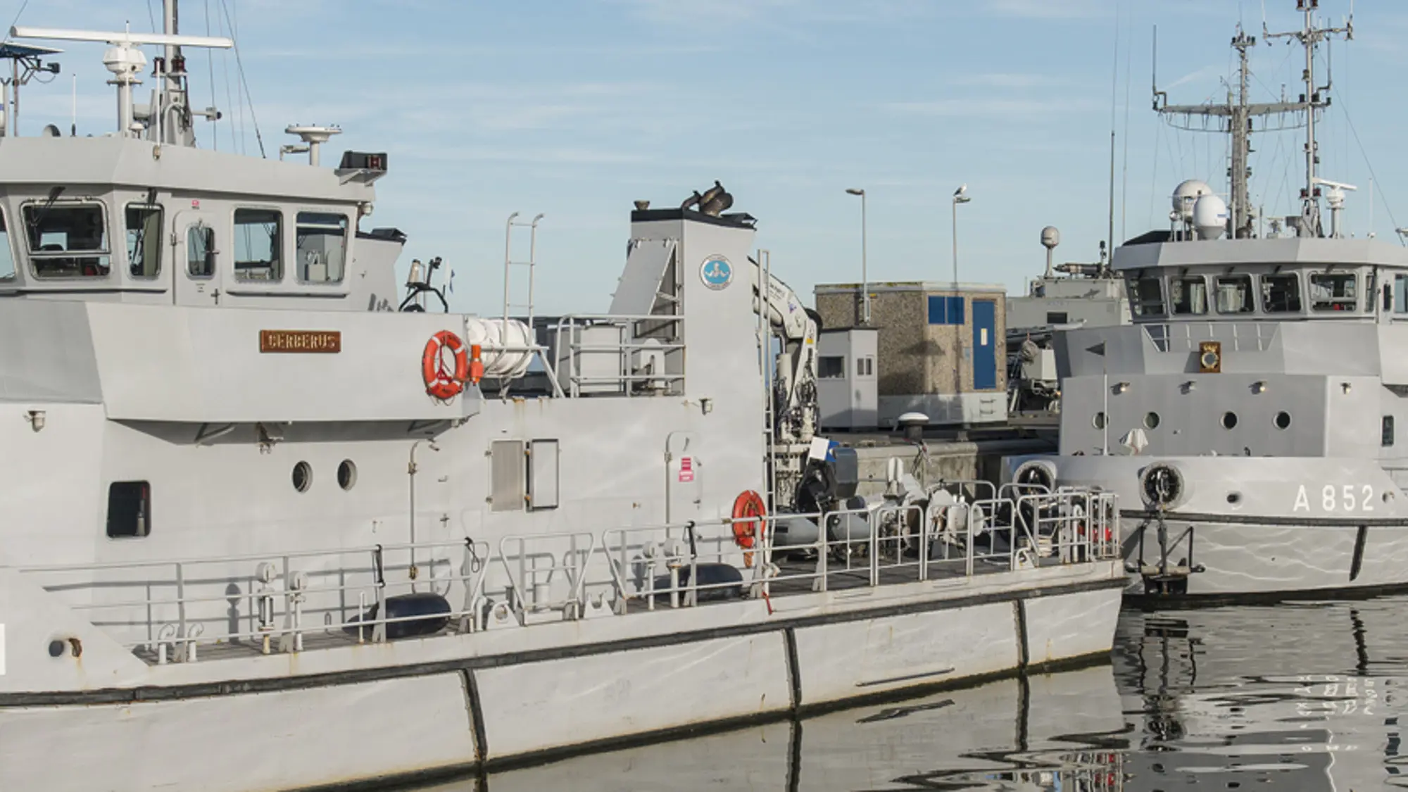 Drie marineschepen liggen aan de kade.