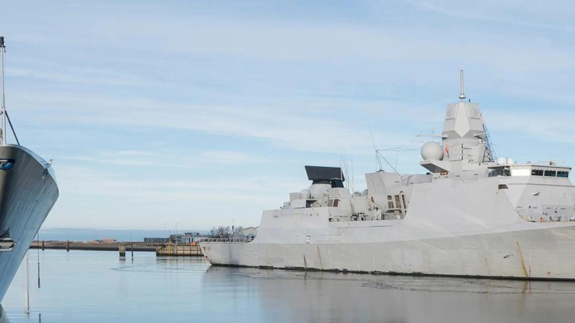 Twee marineschepen liggen aangemeerd in de haven.
