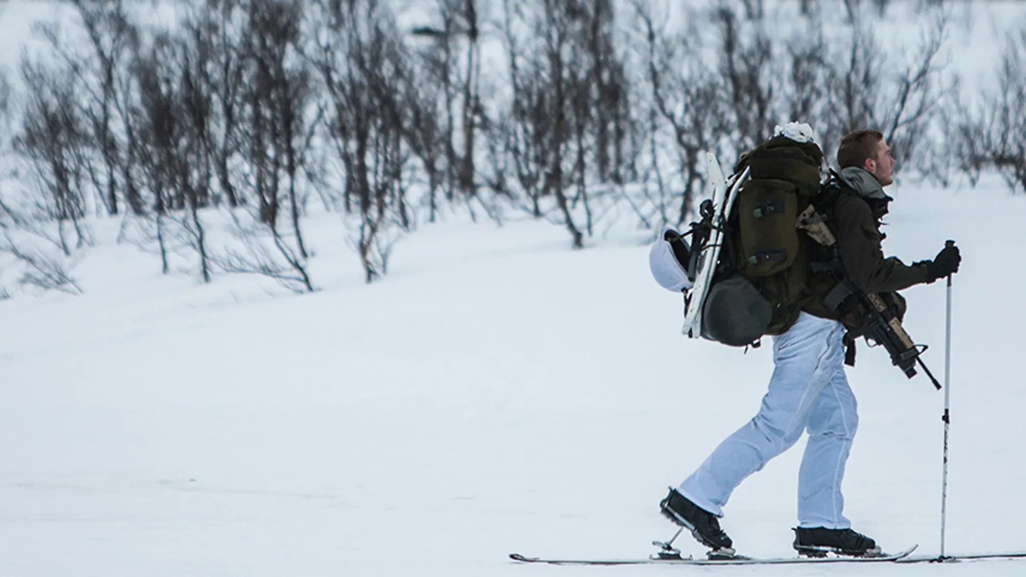 Drie mariniers met volle bepakking op ski's in de sneeuw.