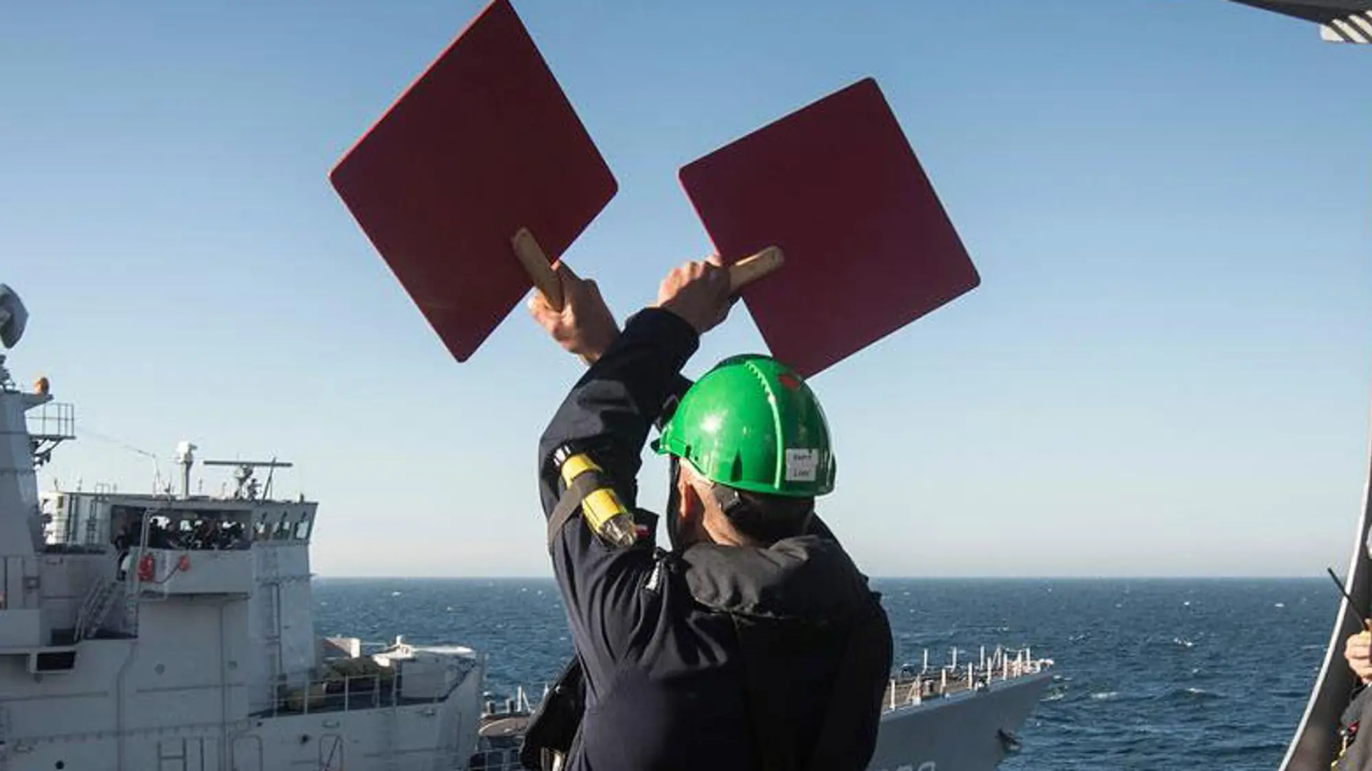 Militair seint vanaf het ene marineschip naar een ander marineschip door 2 rode borden omhoog te houden.