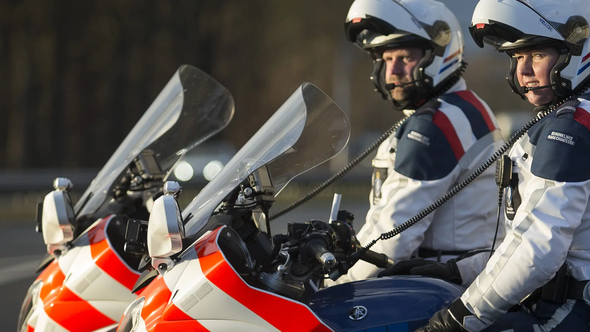 Twee motorrijders van de KMar staan naast elkaar stil.