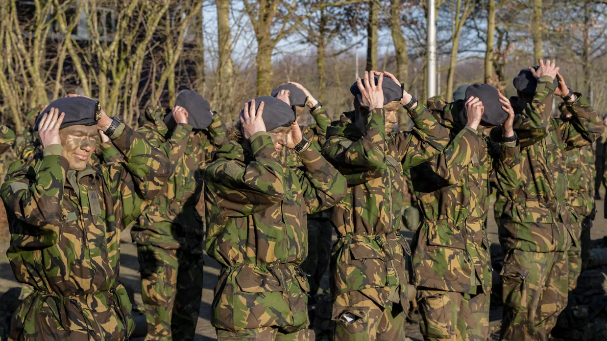In rijen opgestelde militairen zetten hun baret op.