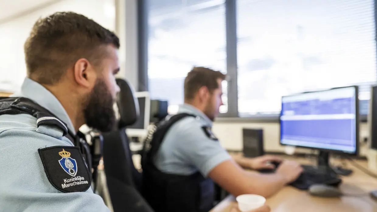 Twee marechaussees kijken naar het PC-scherm.