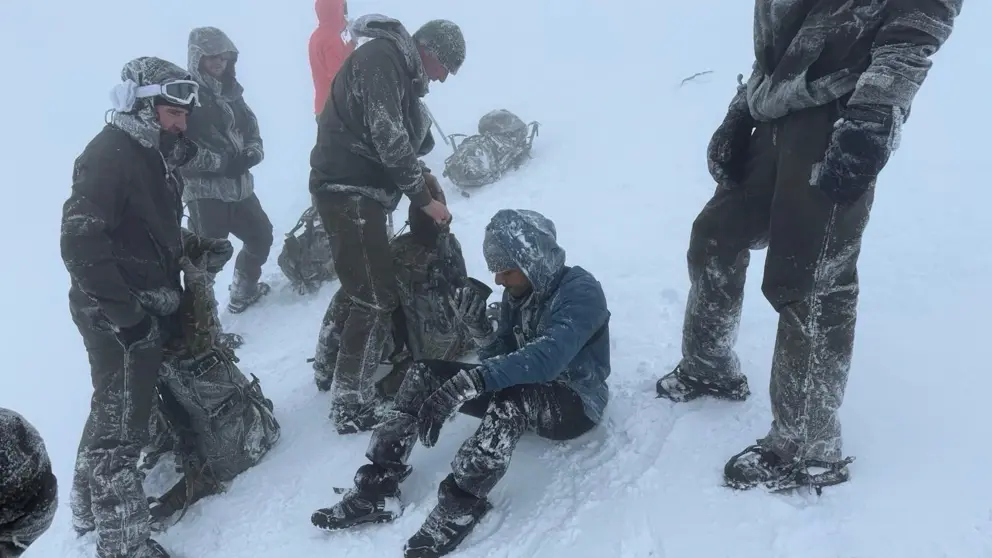 Mariniers staan in de sneeuw om een man heen die op de grond zit en uit een beker drinkt. 