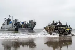 LCU-landingsvaartuig ligt vlakbij het strand, en een Fennek-verkenningsvoertuig met 2 militairen erin rijdt op de voorgrond. 