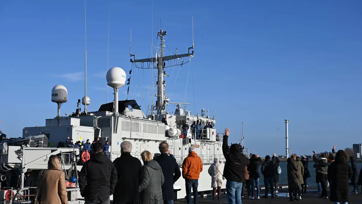 Mensen zwaaien een vertrekkend marineschip uit.