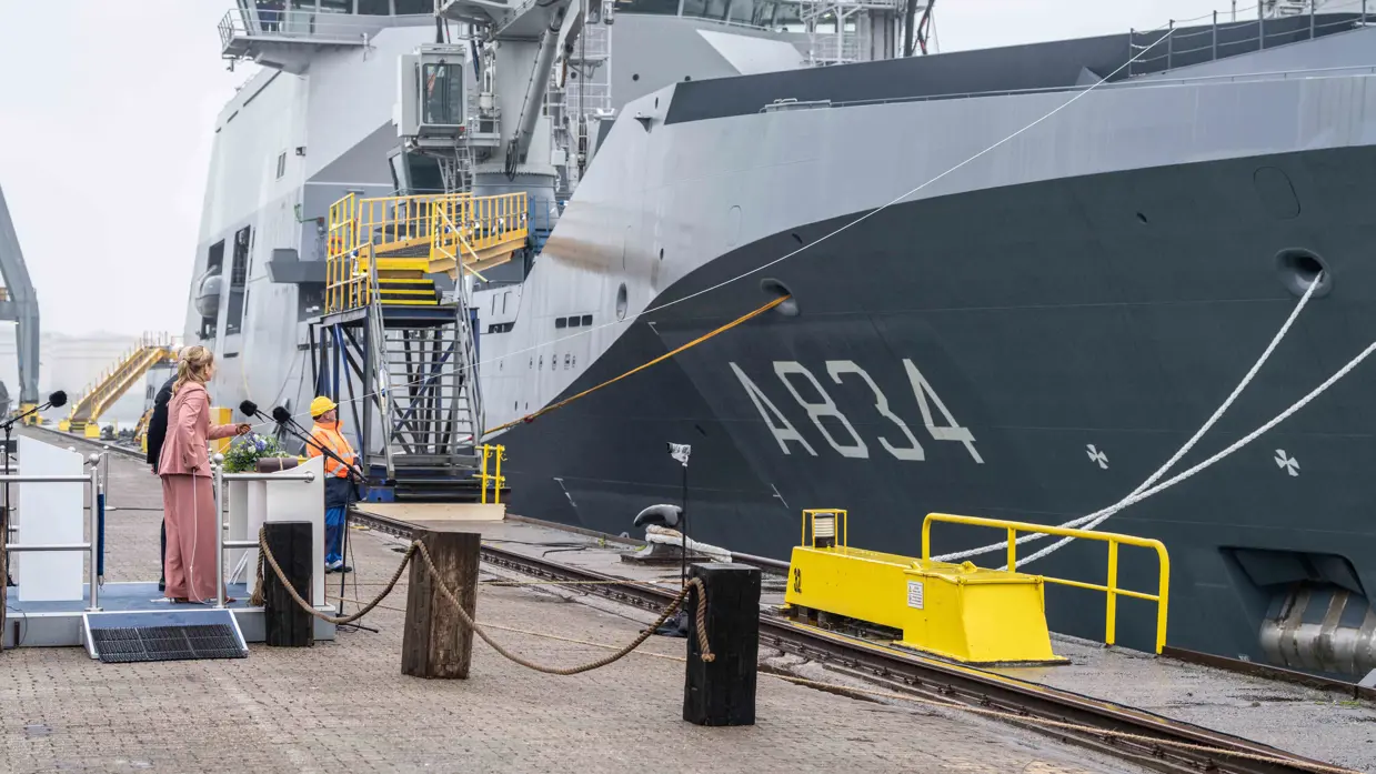Kroonprinses Amalia staat op de kade om marineschip te dopen met champagne.