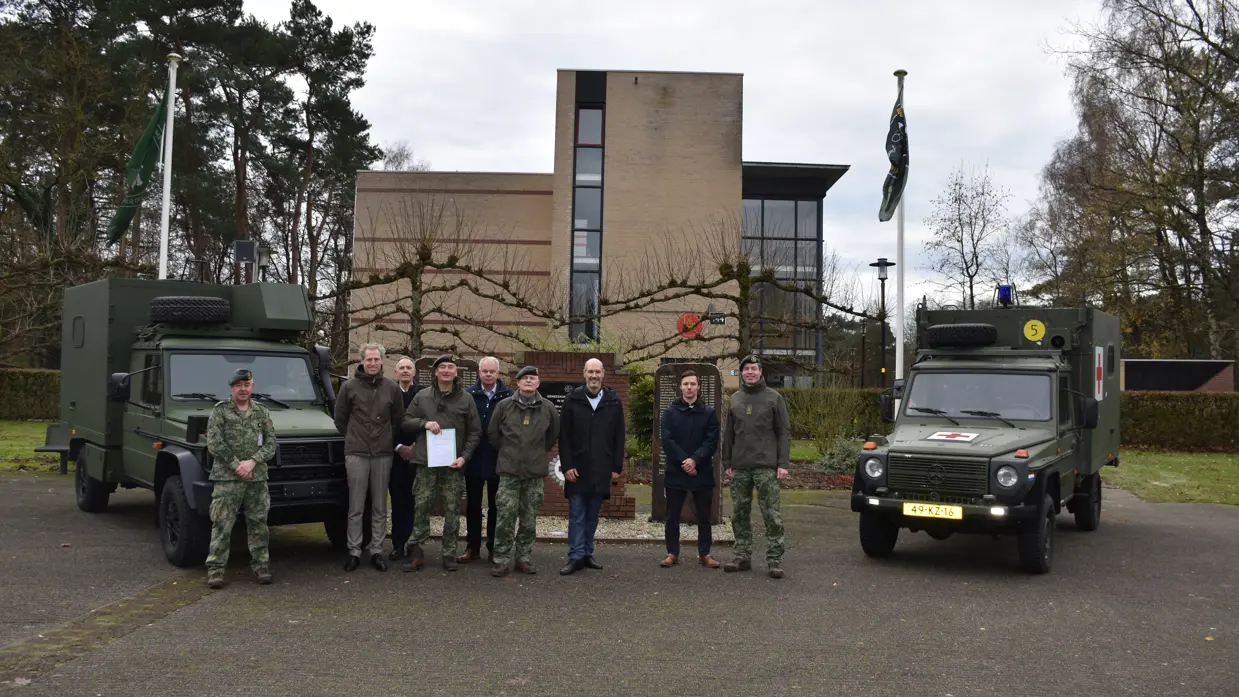 Alttekst: Burgers en militairen poseren op een plein voor twee militaire voertuigen.