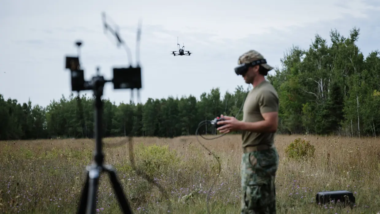 Een marinier stuurt en volgt een drone met een controller en een FPV-bril. Op de voorgrond staat een zendmastje.