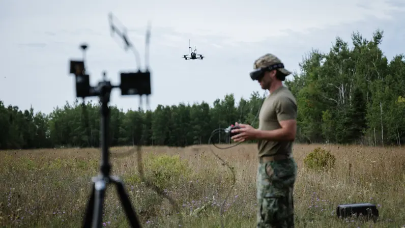 Een marinier stuurt en volgt een drone met een controller en een FPV-bril. Op de voorgrond staat een zendmastje.