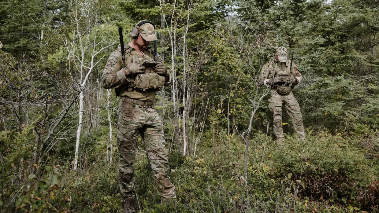 2 mariniers bij een bosrand kijken op het scherm van hun transferradio.