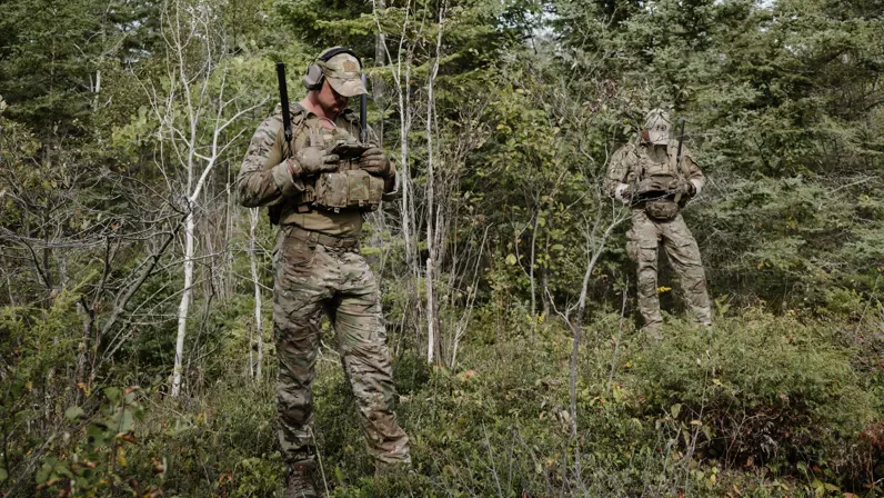 2 mariniers bij een bosrand kijken op het scherm van hun transferradio.