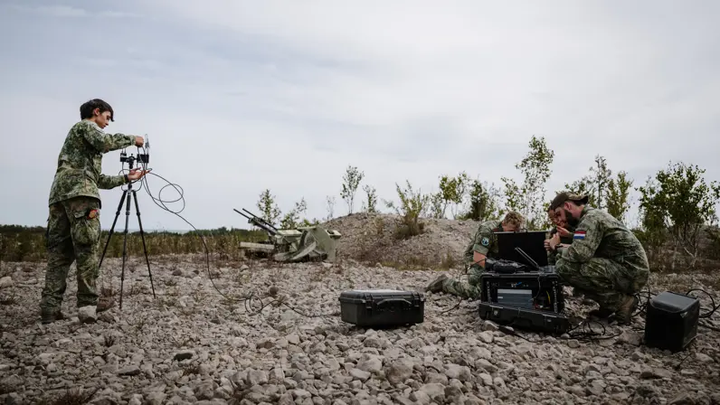 3 zittende militairen en 1 staand op stenen bekommeren zich over hun apparatuur.