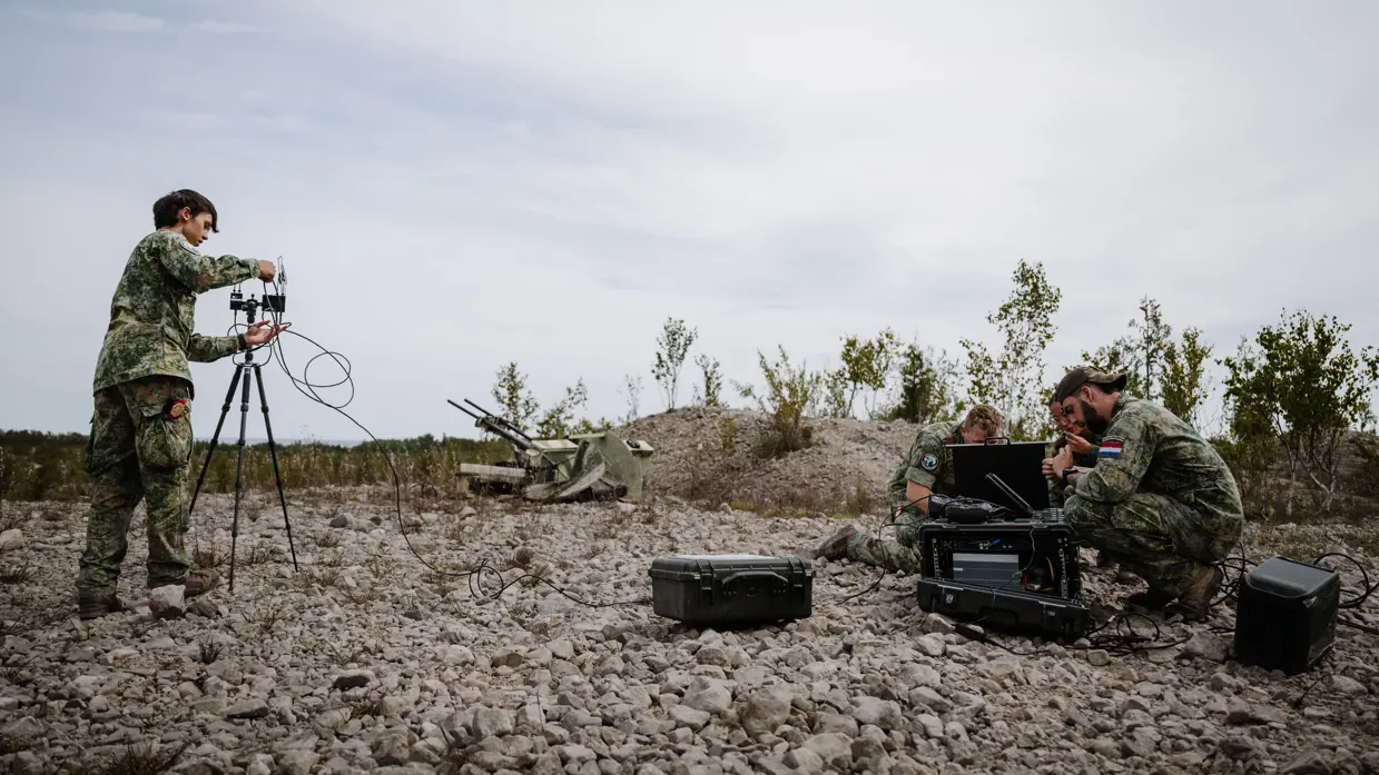 3 zittende militairen en 1 staand op stenen bekommeren zich over hun apparatuur.