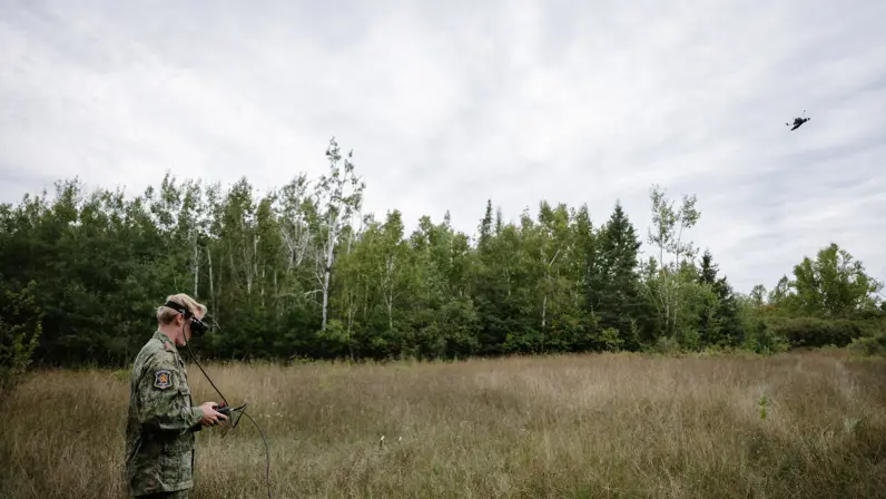 Een militair met FPV-monitor in handen houdt in het bos zijn vliegende drone in de gaten.