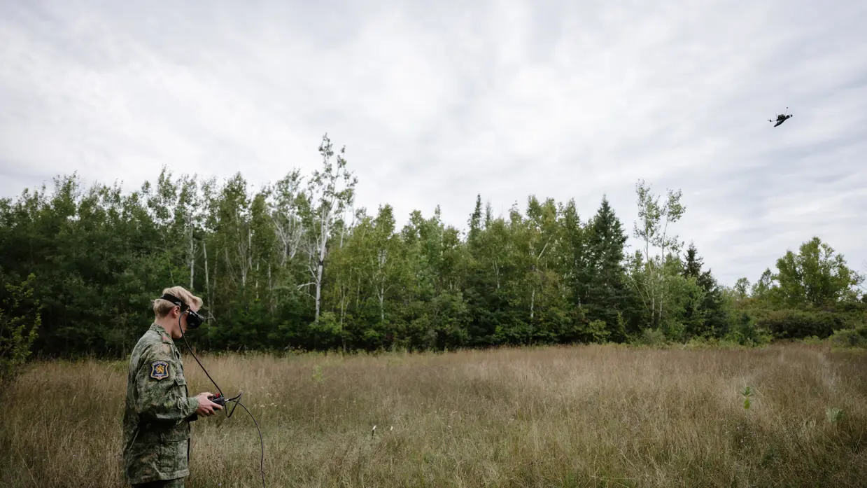 Een militair met FPV-monitor in handen houdt in het bos zijn vliegende drone in de gaten.