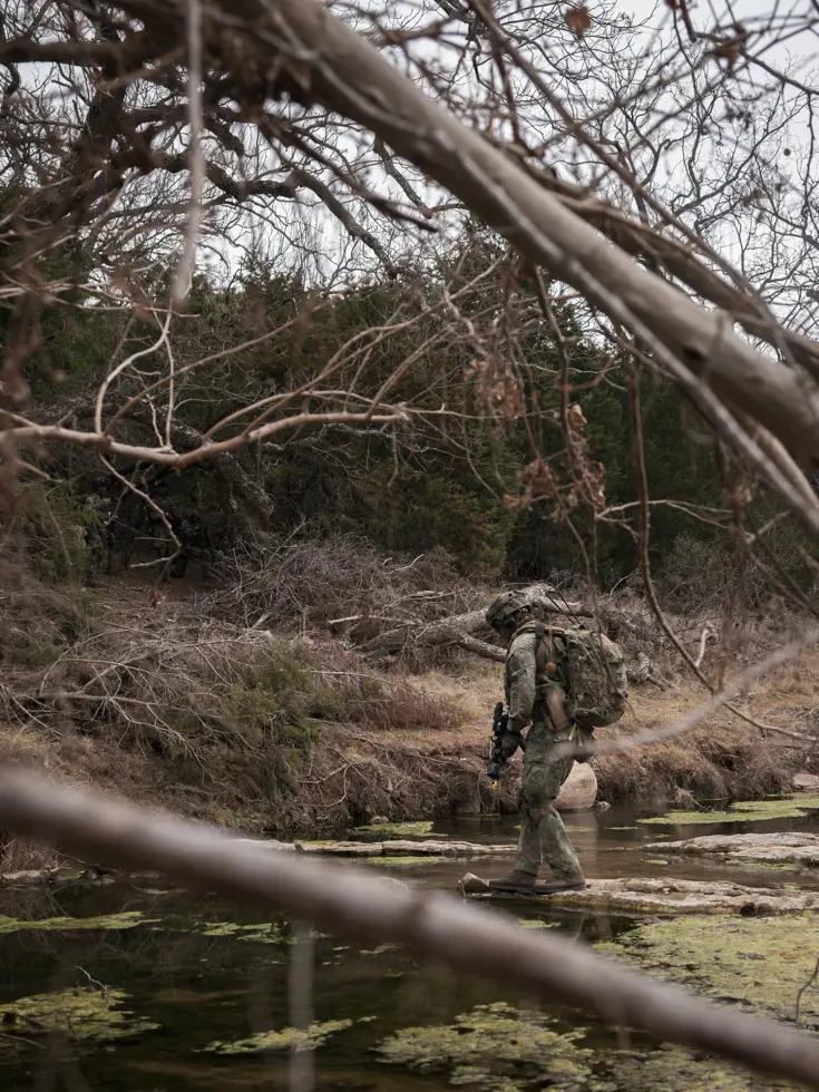 Militair steekt via lage rotsen een rivier over.