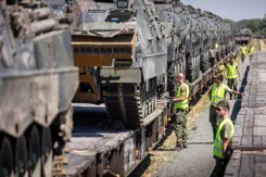 Militairen inspecteren tank die op een wagon staan.