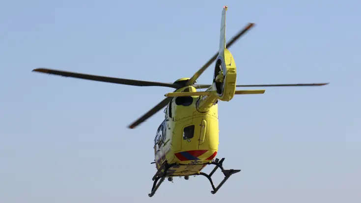  Een kleine gele helikopter vliegt weg onder een blauwe hemel.