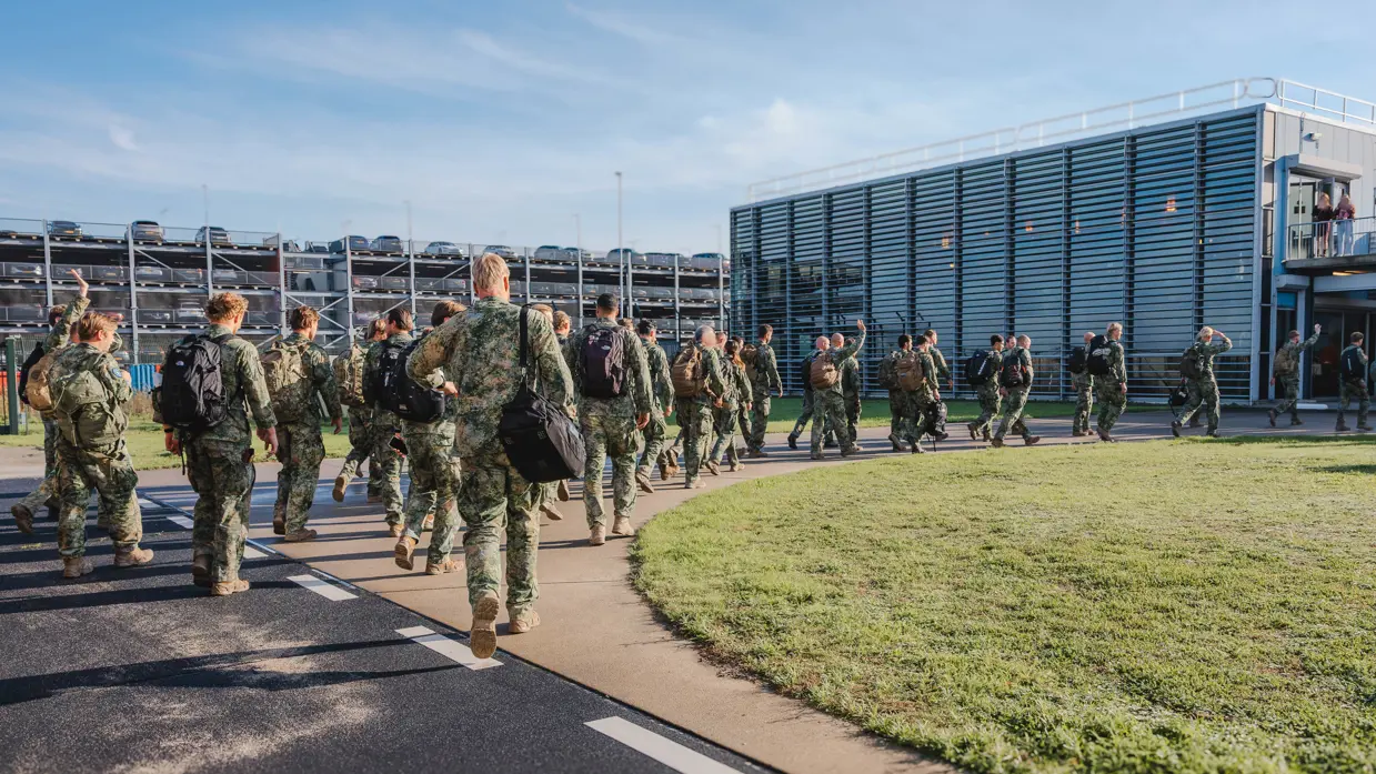 Militairen lopen achter elkaar van landingsband richting terminal.