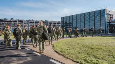 Militairen lopen achter elkaar van landingsband richting terminal.