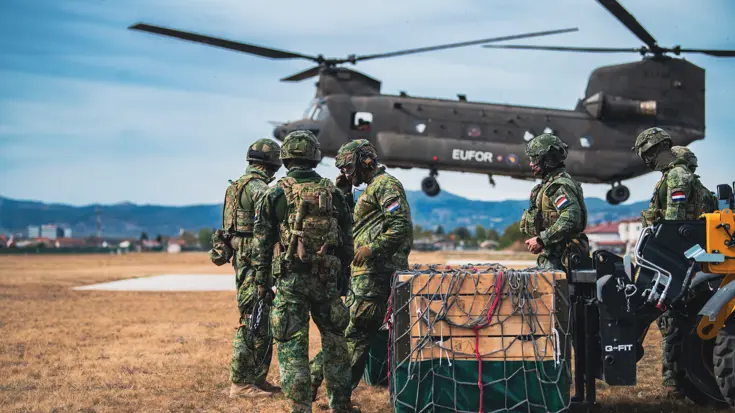 Militairen staan op een veld naast een helikopter.
