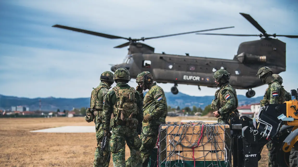 Militairen staan op een veld naast een helikopter.
