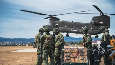 Militairen staan op een veld naast een helikopter.