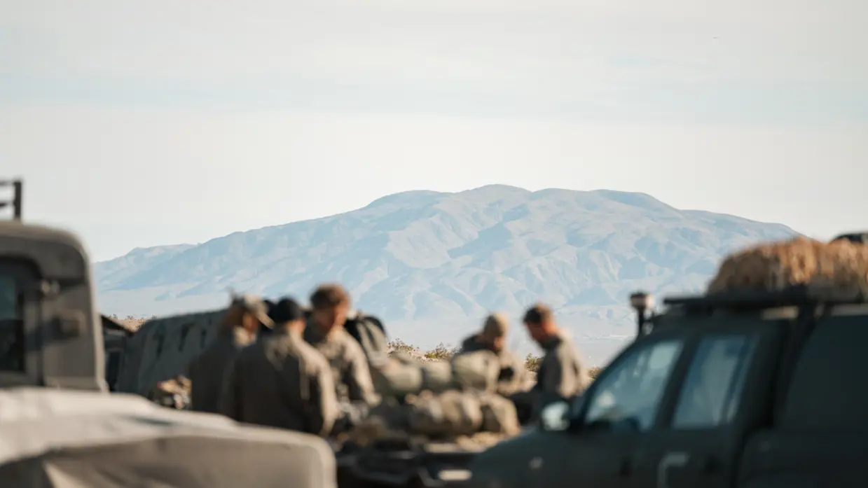 Een groep militairen met op de achtergrond een berg in de Mojave-woestijn. 
