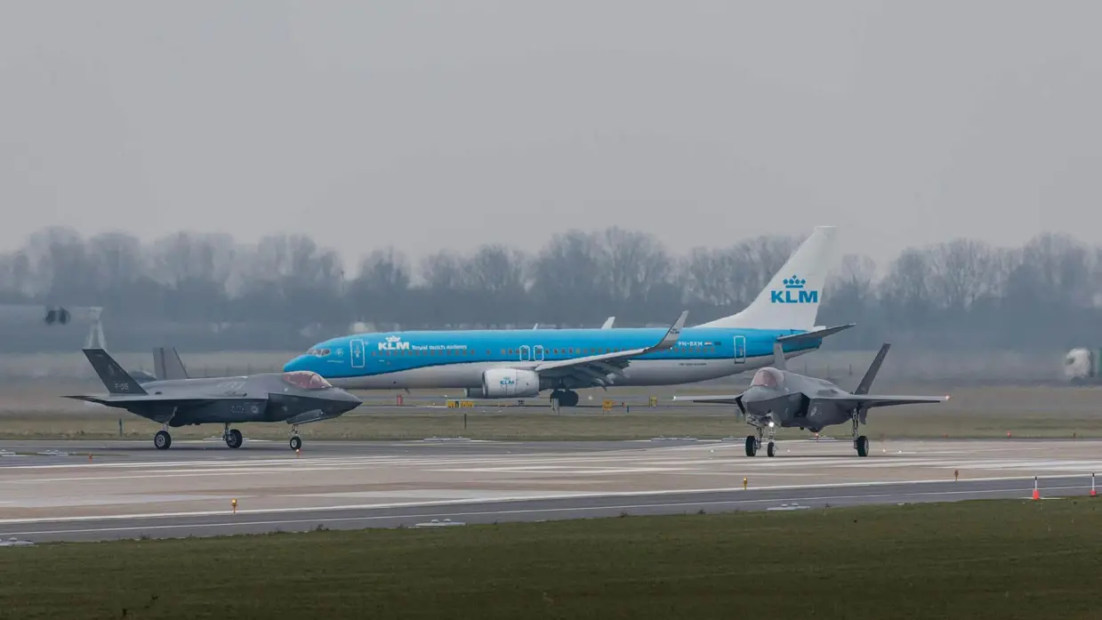 Twee F-35’s taxiën voor een KlM-vliegtuig langs
