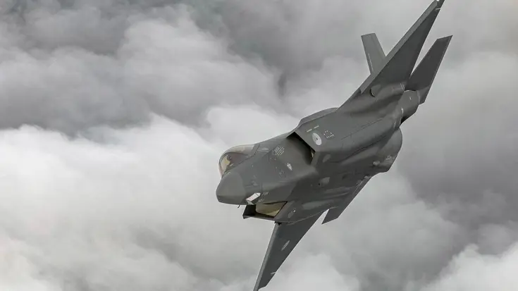 F-35 schuin in een bocht met op achtergrond dik grijs wolkendek.