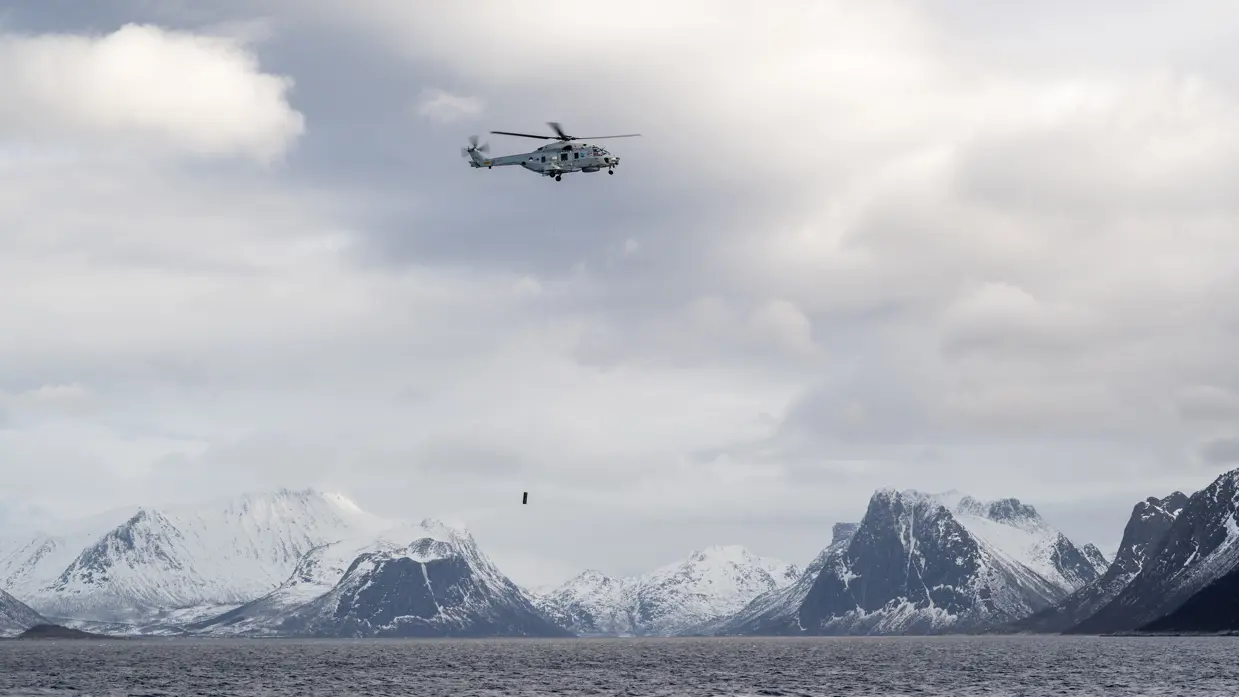 Alttekst: Een NH90 die tegen de achtergrond van besneeuwde rotsen haar sonar te water laat. &nbsp; &nbsp;&nbsp;