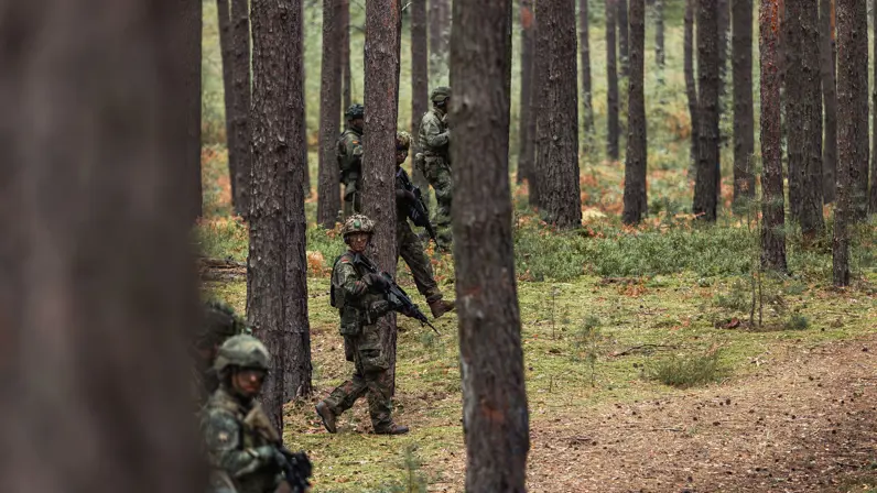 militairen met het wapen in de aanslag lopend door het bos.&nbsp;