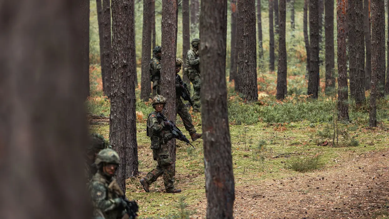 militairen met het wapen in de aanslag lopend door het bos.&nbsp;