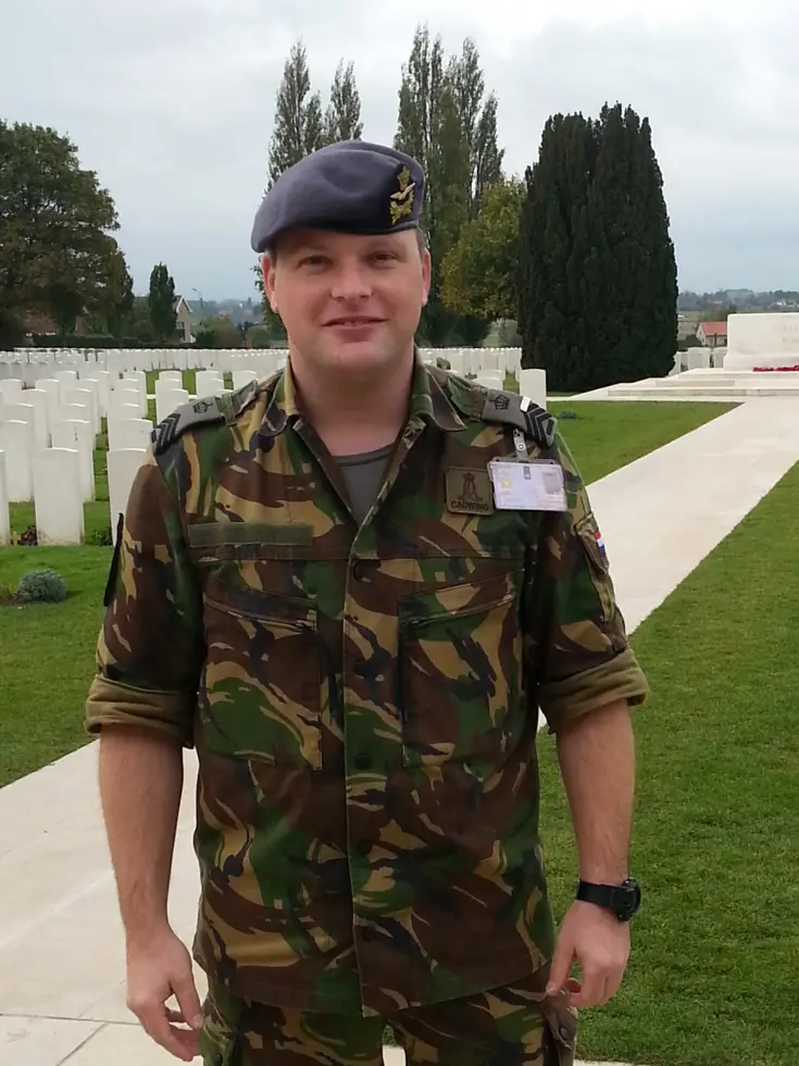 Een jonge Tim Nelissen in gevechtstenue staat op een militaire begraafplaats met witte grafstenen.
