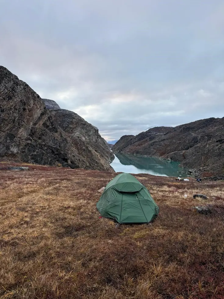 Een groen tentje bovenop een berg met uitzicht op een weids fjord. 