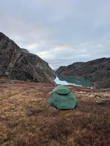 Een groen tentje bovenop een berg met uitzicht op een weids fjord. 