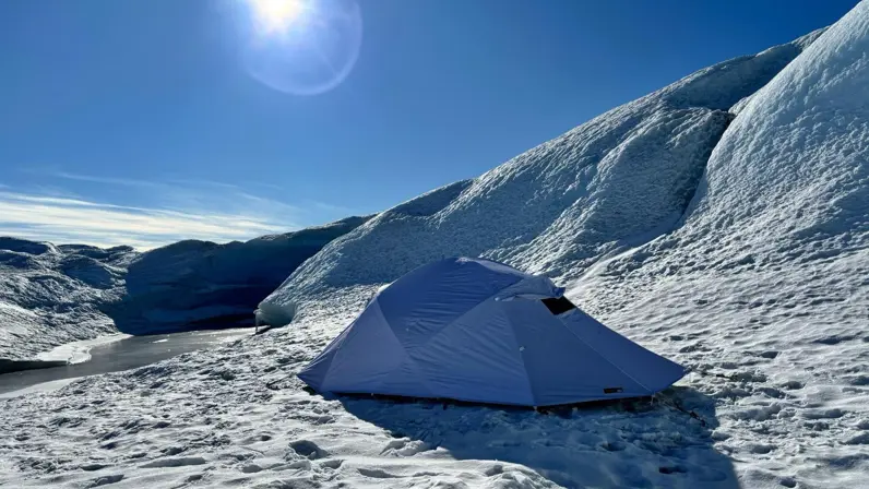 Een witte koudweer-tent staat in de sneeuw onder een strakblauwe lucht.