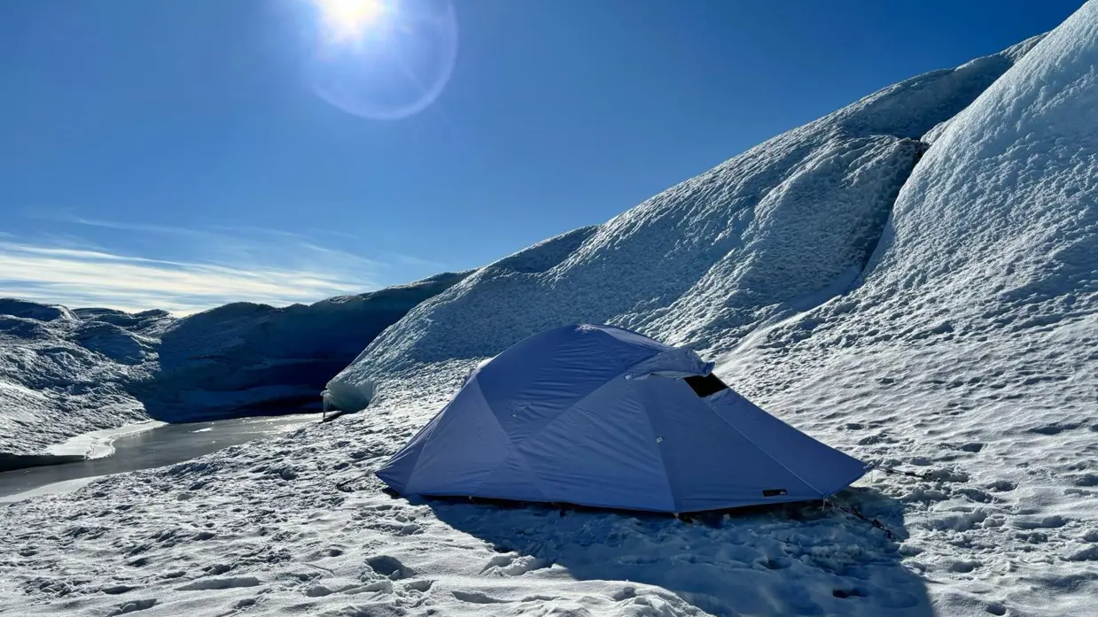 Een witte koudweer-tent staat in de sneeuw onder een strakblauwe lucht.